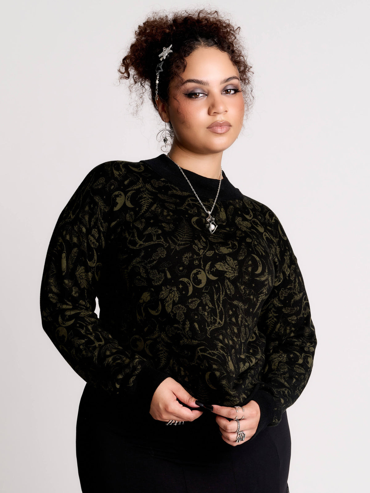 a black long-sleeve top with an intricate olive green forest findings pattern