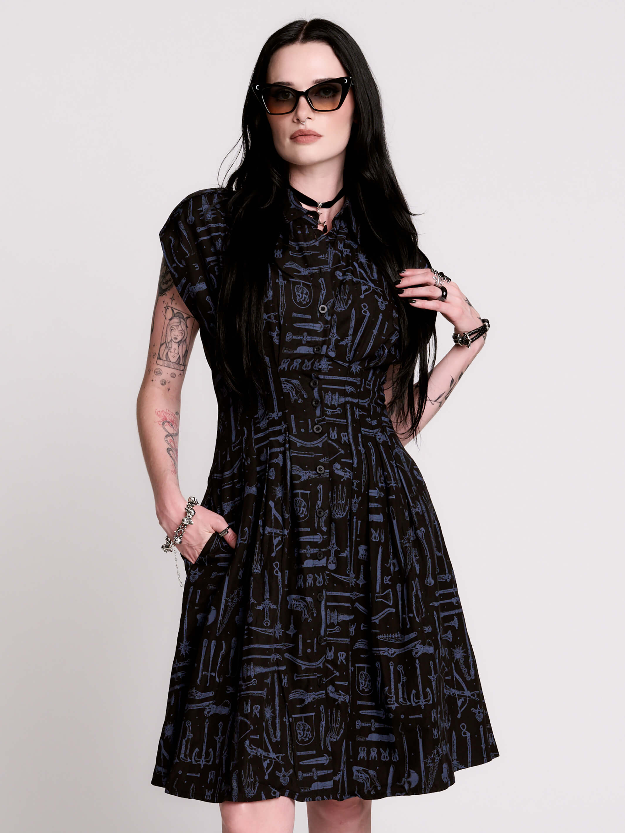 a button-front shirt dress featuring a striking medieval-inspired print with weaponry and macabre motifs.