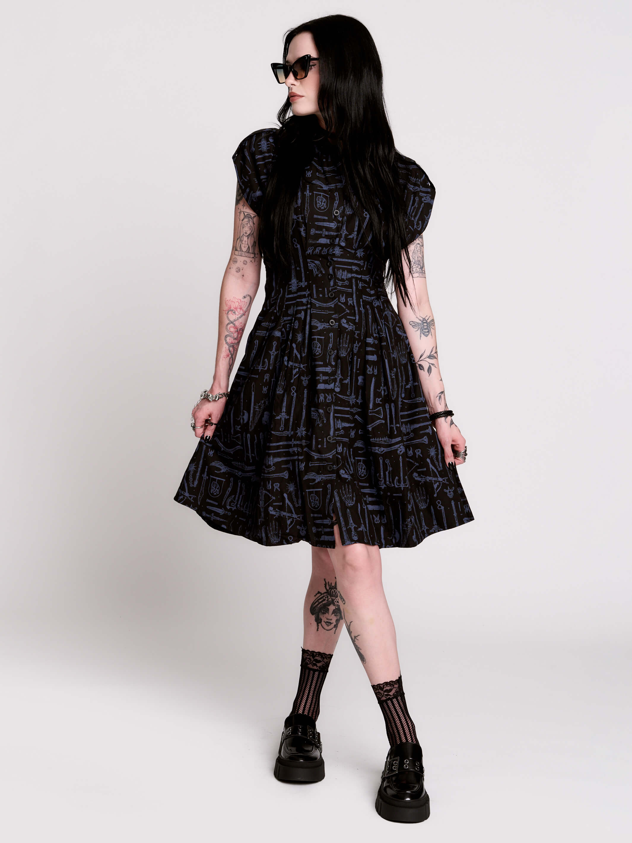 a button-front shirt dress featuring a striking medieval-inspired print with weaponry and macabre motifs.