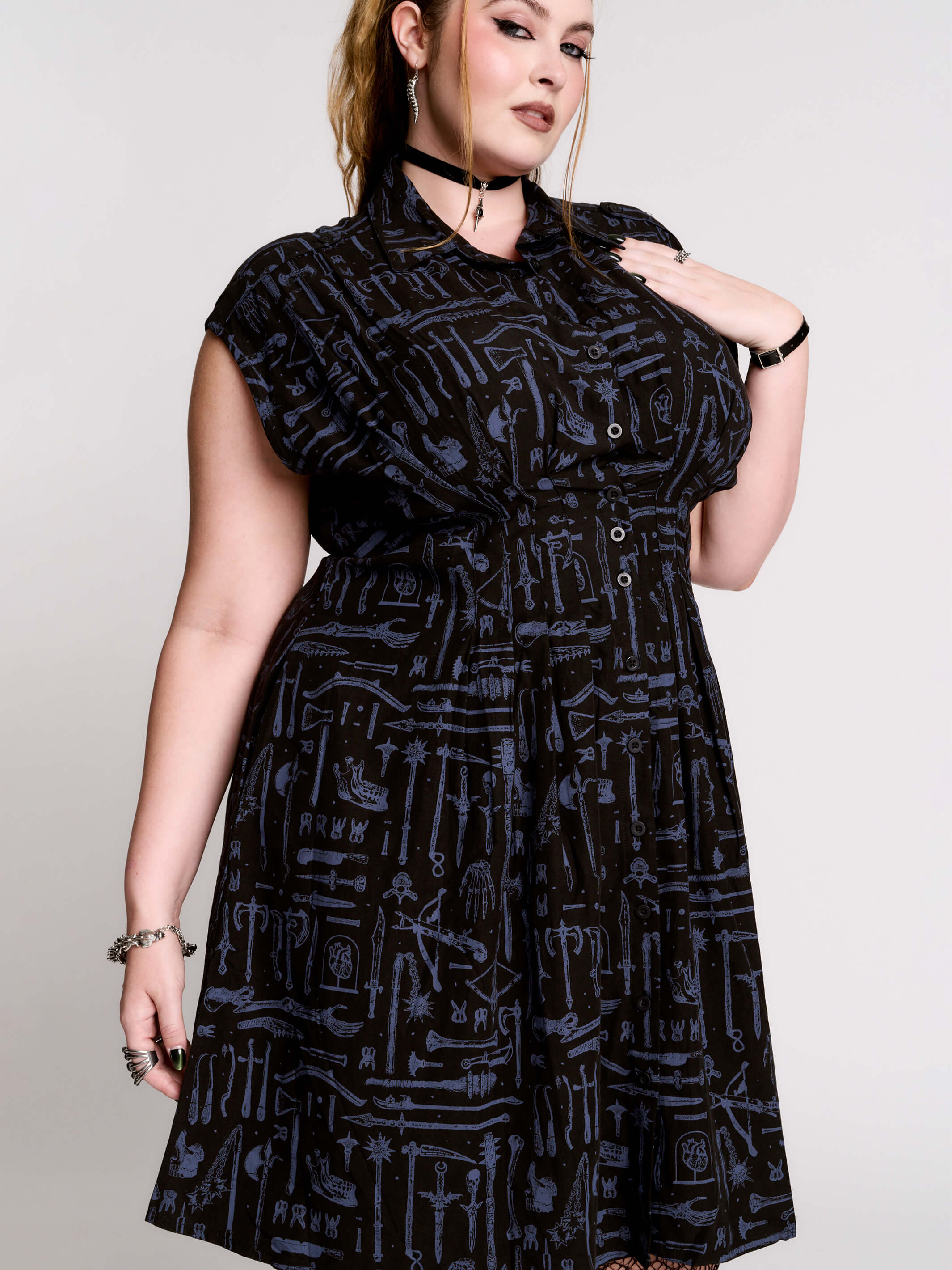a button-front shirt dress featuring a striking medieval-inspired print with weaponry and macabre motifs.
