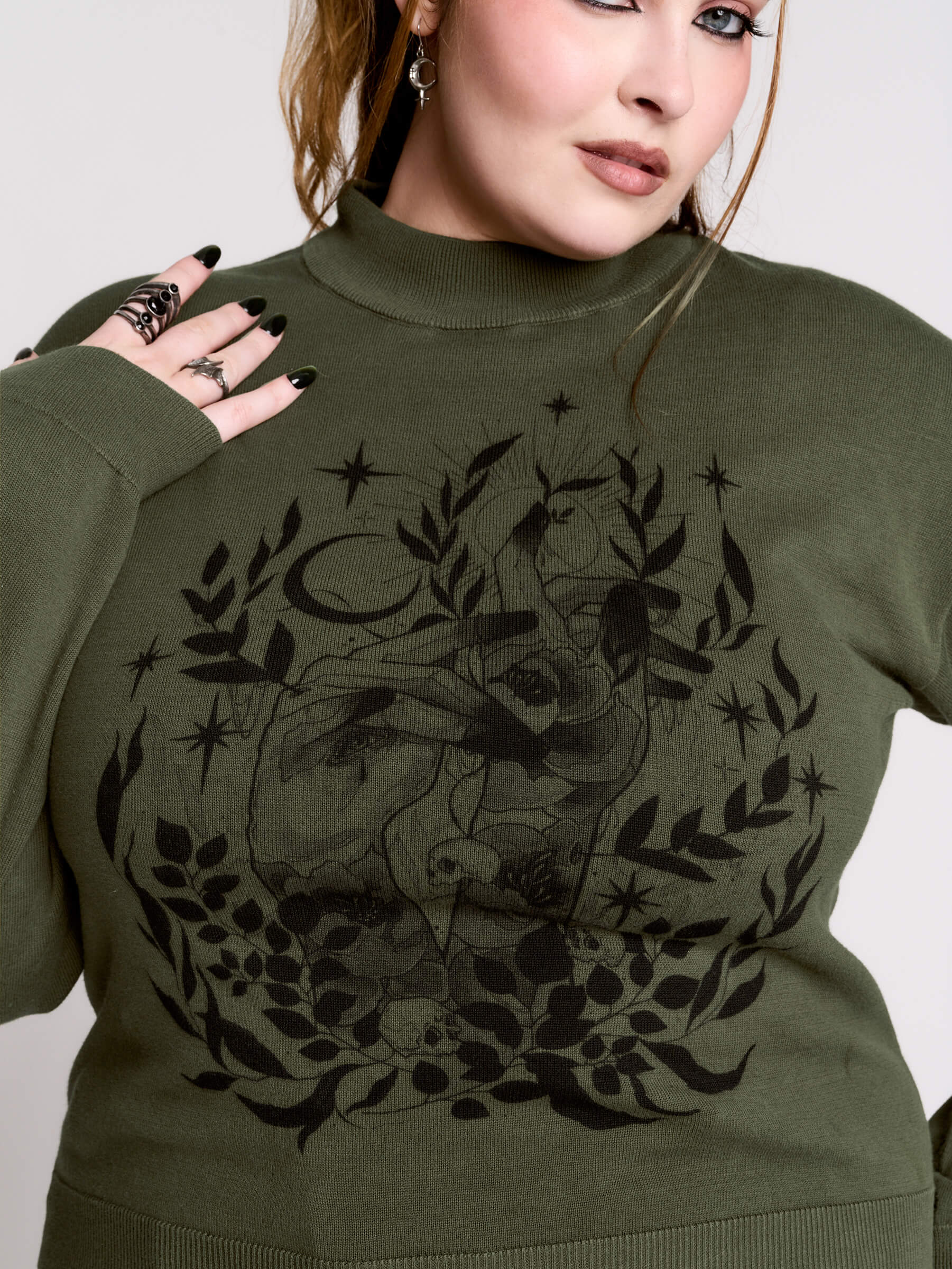 an olive green mock-neck sweater featuring a black gothic graphic