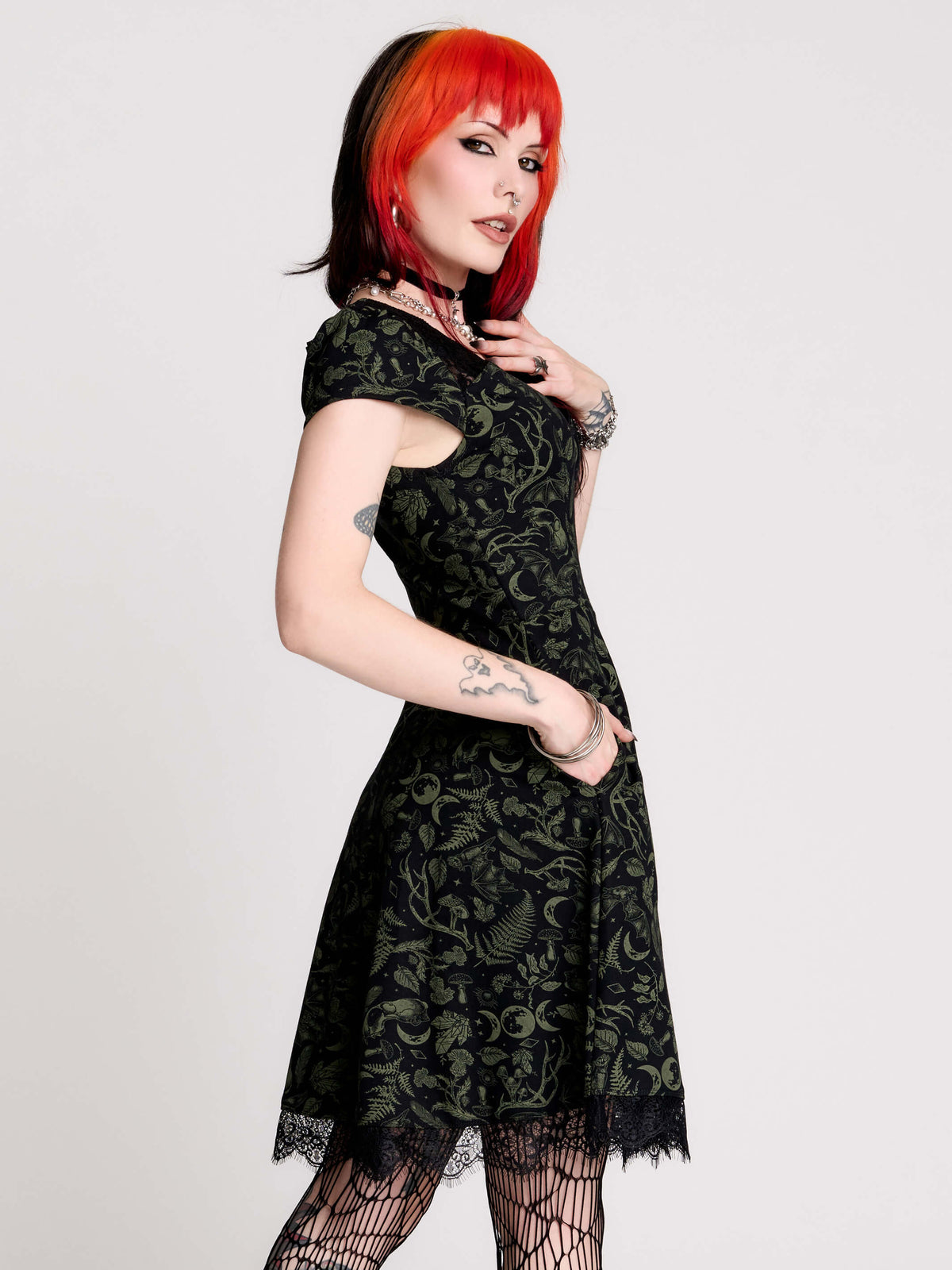 short black dress with a green leafy lace pattern, featuring cap sleeves, a V-neckline, side pockets, and a scalloped lace hem.