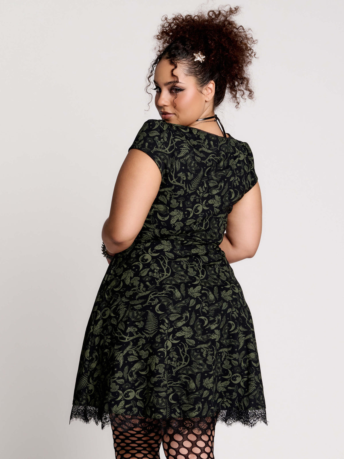 short black dress with a green leafy lace pattern, featuring cap sleeves, a V-neckline, side pockets, and a scalloped lace hem.