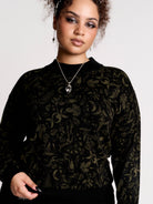 a black long-sleeve top with an intricate olive green forest findings pattern