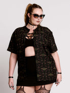 a black short-sleeve button-up shirt with a dark green and pink occult-style pattern.