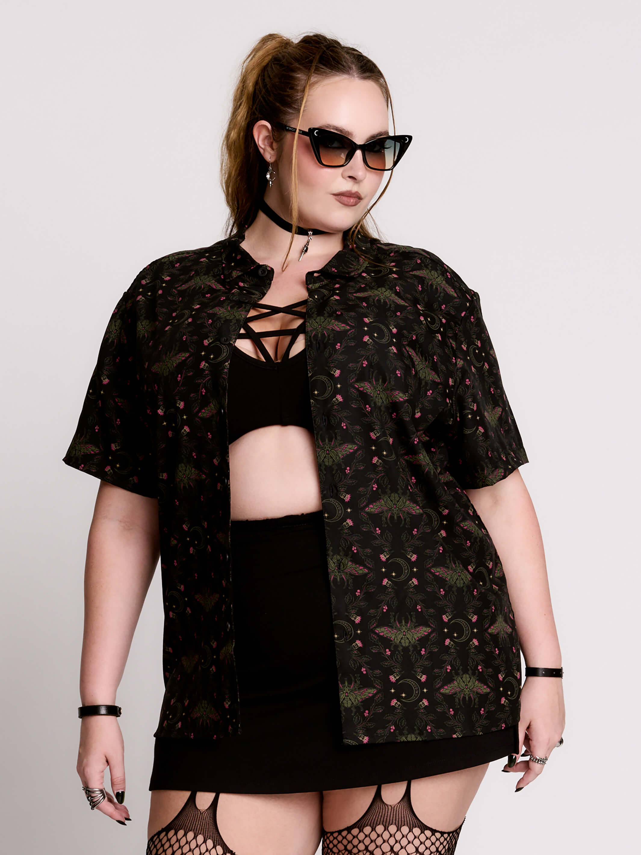 a black short-sleeve button-up shirt with a dark green and pink occult-style pattern.