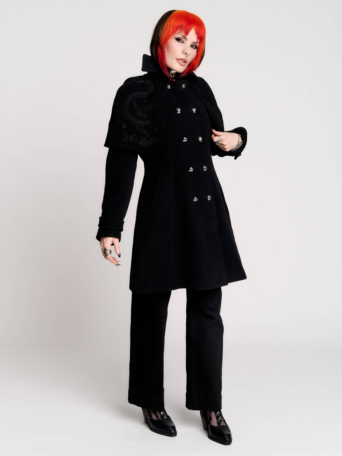 a black double-breasted coat with silver buttons and gothic dragon embroidery on the shoulder cape