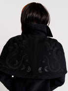 a black double-breasted coat with silver buttons and gothic dragon embroidery on the shoulder cape