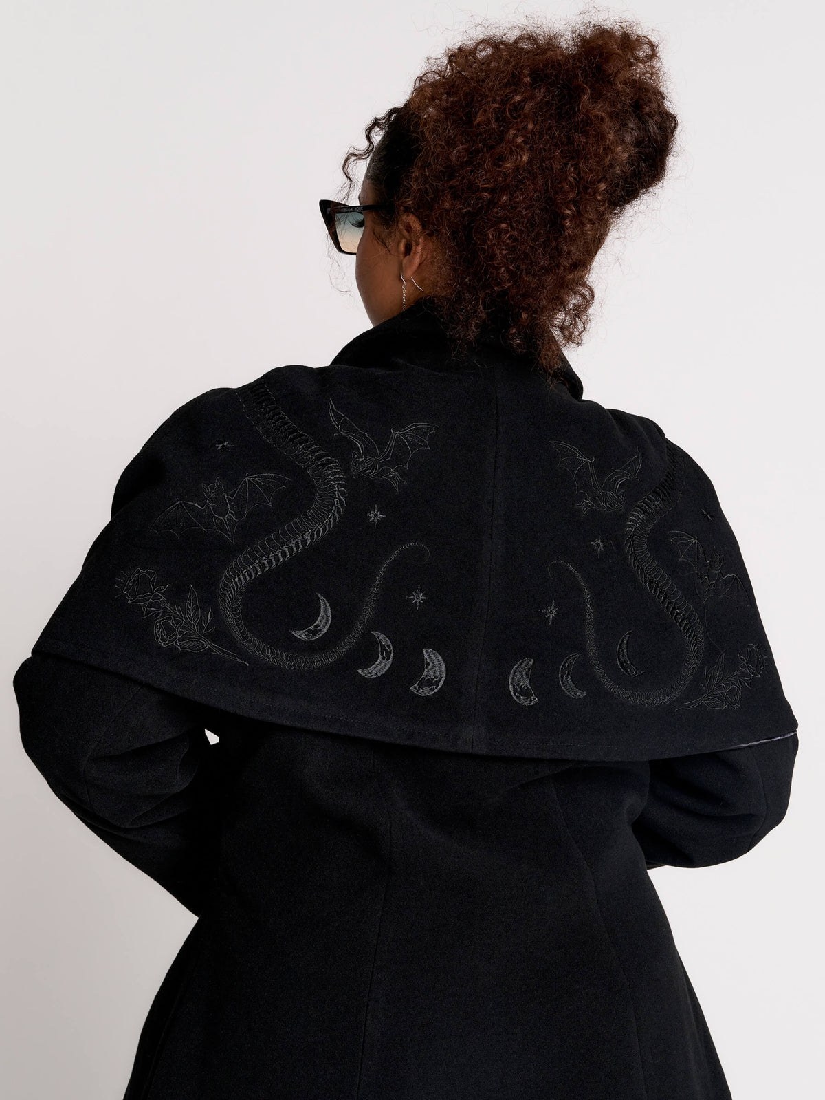 a black double-breasted coat with silver buttons and gothic dragon embroidery on the shoulder cape