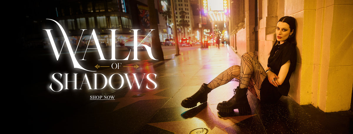 A promotional banner for 'Walk of Shadows' featuring a woman sitting on a city sidewalk at night, leaning against a wall. The left side features the title 'Walk of Shadows' in large white gothic lettering with a 'SHOP NOW' link below it.