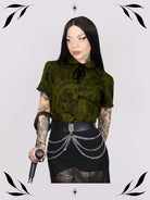 a short-sleeve olive green blouse with a dark botanical pattern, black lace trim collar with black ribbon tiedetail and black buttons. 