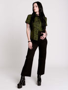 a short-sleeve olive green blouse with a dark botanical pattern, black lace trim collar with black ribbon tiedetail and black buttons. 