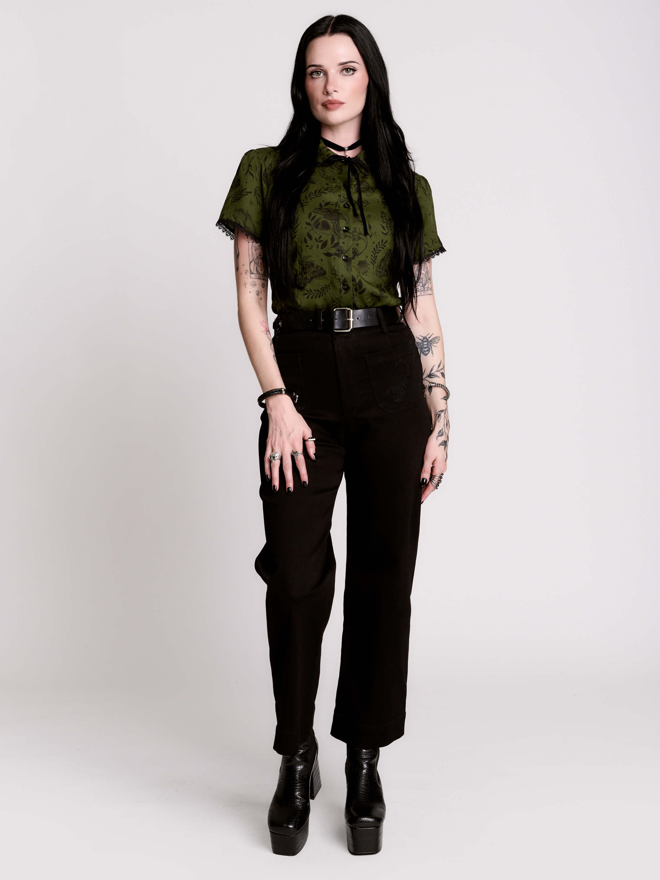 a short-sleeve olive green blouse with a dark botanical pattern, black lace trim collar with black ribbon tiedetail and black buttons. 