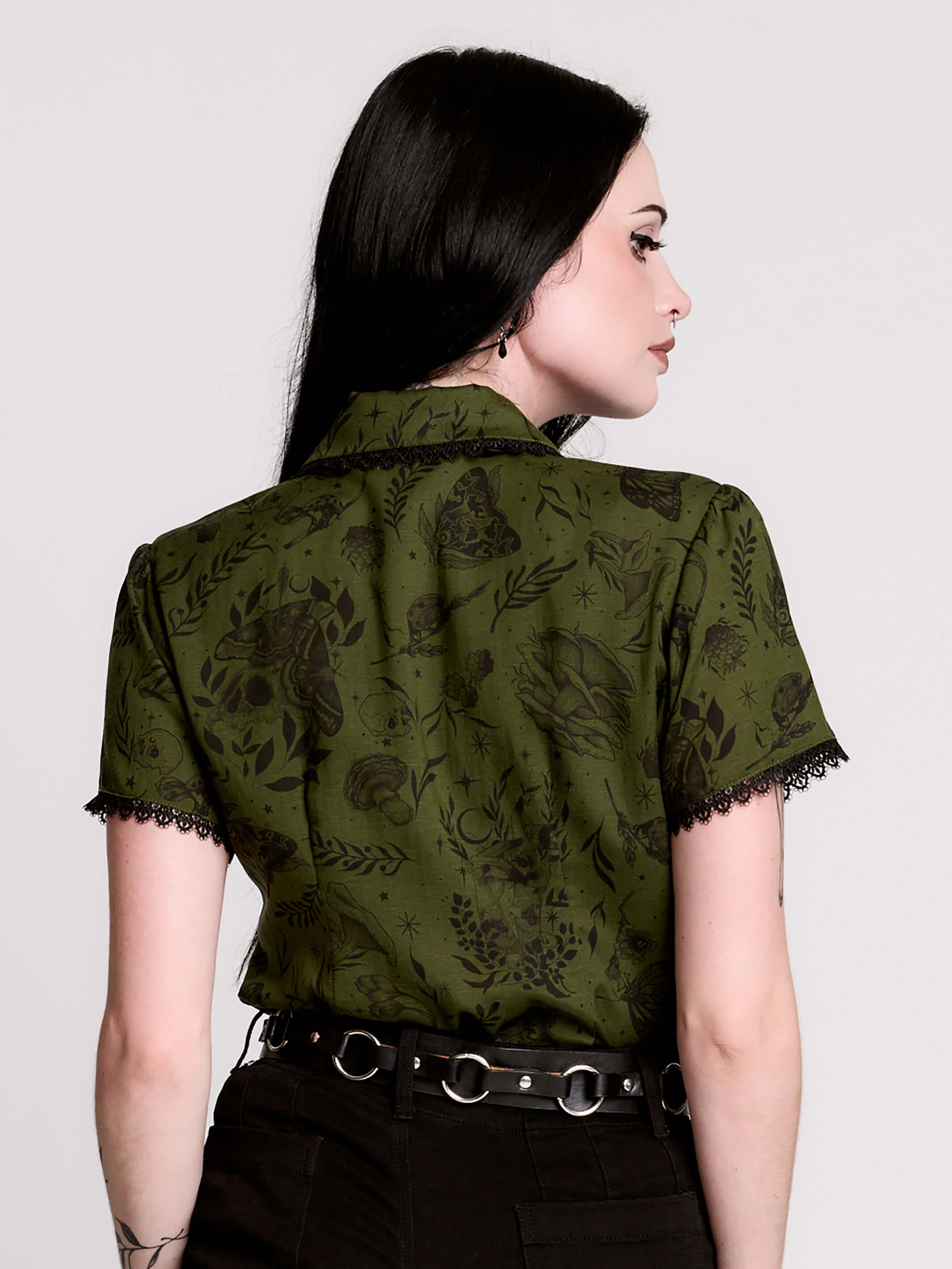 a short-sleeve olive green blouse with a dark botanical pattern, black lace trim collar with black ribbon tiedetail and black buttons. 
