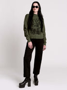 an olive green mock-neck sweater featuring a black gothic graphic