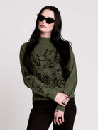an olive green mock-neck sweater featuring a black gothic graphic